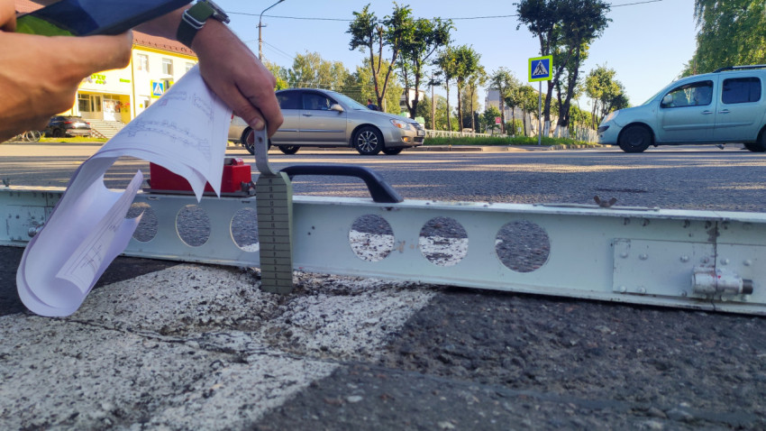 Клин-щуп и металлическая рейка измеряют перепад на асфальте рядом с полосой разметки