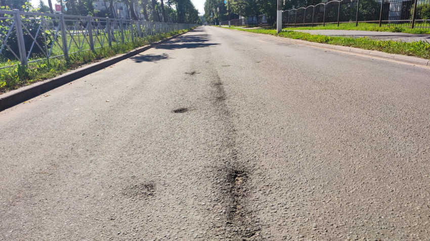 Асфальтовая дорога с заплатками и швами рядом с тротуаром и заборами