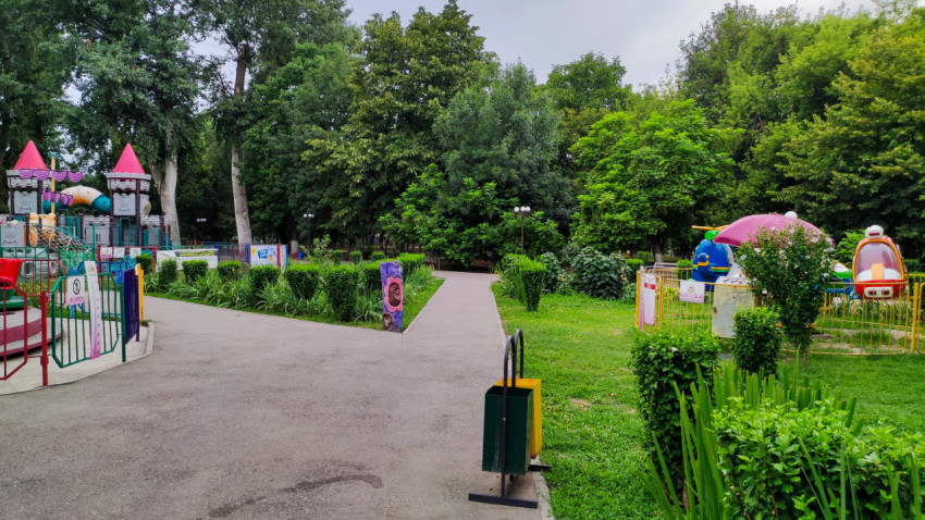 Дорожка в зелёном парке ведёт между детскими аттракционами и газонами