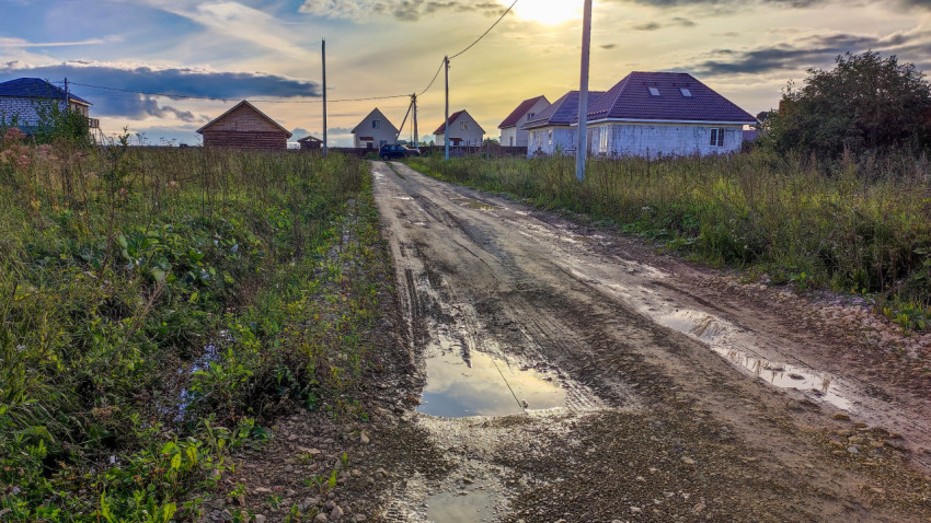 Гравийная дорога в коттеджном поселке с лужами после дождя