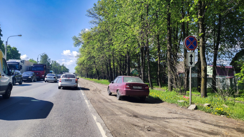 Городская дорога с грунтовой обочиной, знаком запрета остановки и припаркованным авто