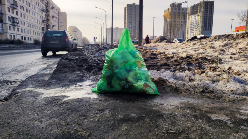 Зеленый пакет с отходами на обочине у дороги