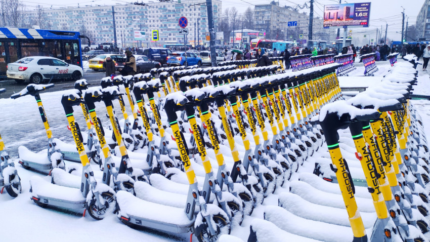 Электросамокаты в снегу на фоне плотного трафика и жилых домов