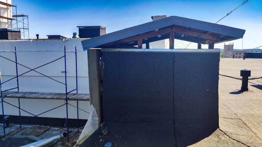 Вентиляционный выход с двускатным металлическим колпаком на плоской крыше рядом со строительными лесами