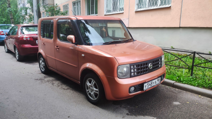Оранжевый Nissan Cube припаркован во дворе у жилого дома
