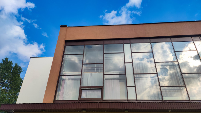 Большие панорамные окна современного здания отражают голубое небо и облака