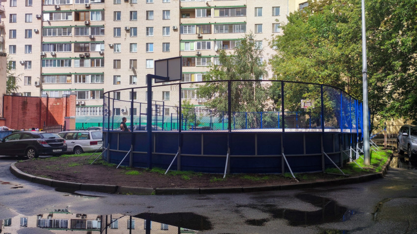 Огороженная спортивная площадка с баскетбольным щитом во дворе жилых домов