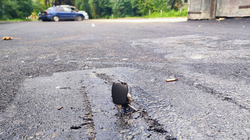 Автомобильный ключ, воткнутый в мягкий битумный шов на асфальте у ограждения во дворе