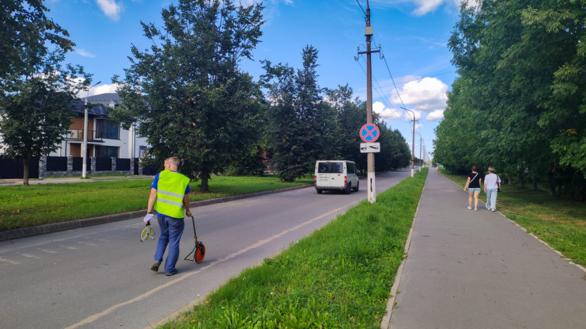Рабочий катит измерительное колесо вдоль улицы под знаком запрета остановки