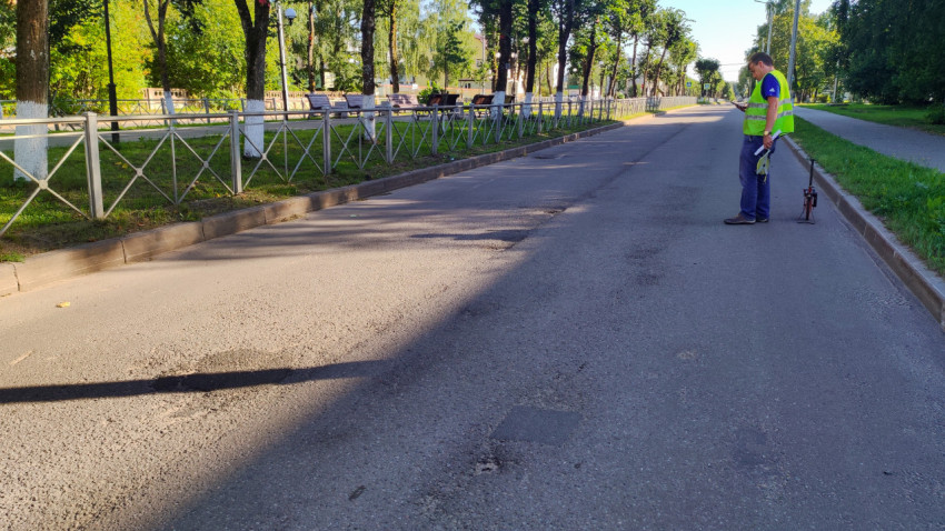 Специалист у обочины стоит с измерительным колесом и прикидывает замер по дороге