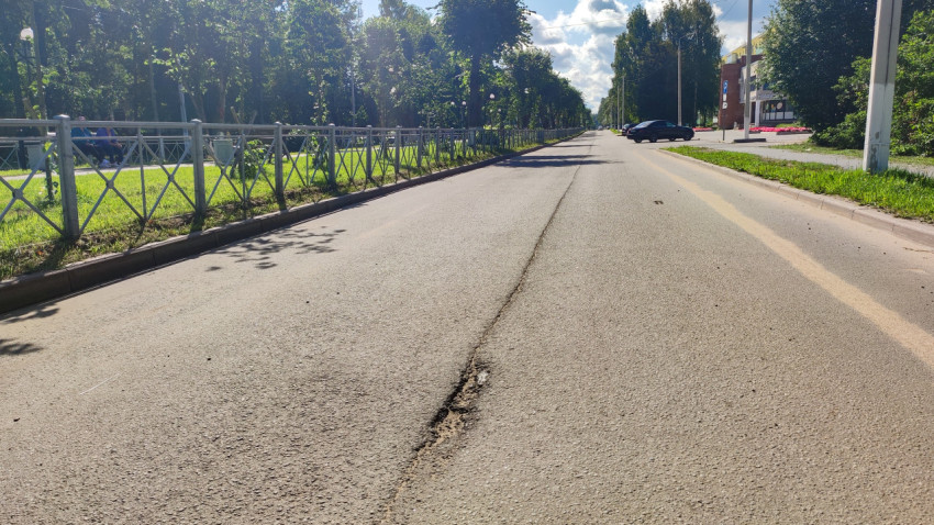 Продольная трещина и осыпание асфальта на городской дороге у парковой аллеи