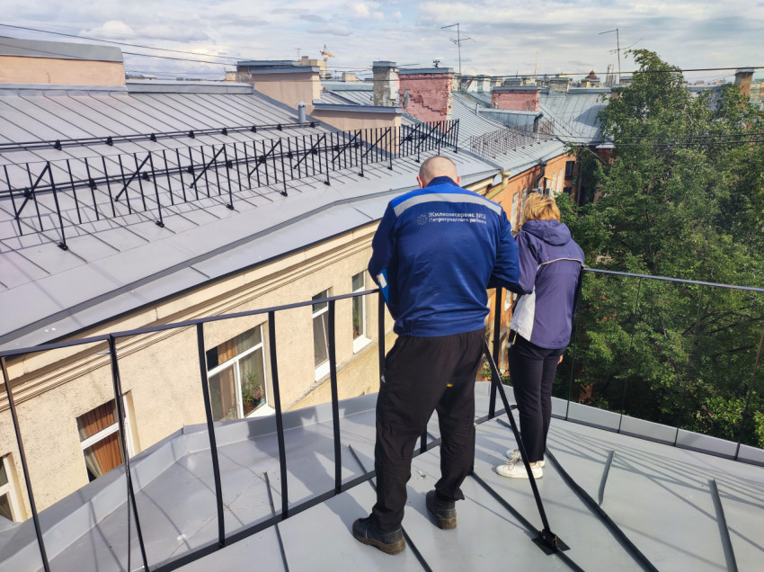 Двое людей на крыше у ограждения на фоне городских крыш и деревьев