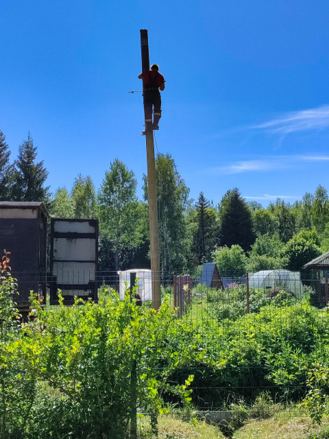 Монтажник работает на высоком столбе связи или электролинии на фоне синего неба