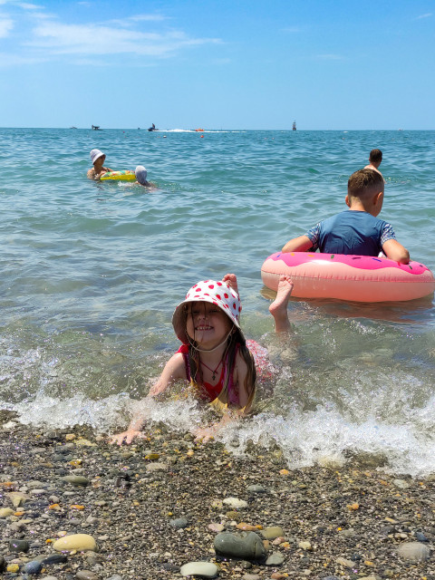 Девочка играет на каменистом пляже у кромки моря