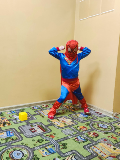 Ребенок в костюме супергероя позирует в игровой комнате