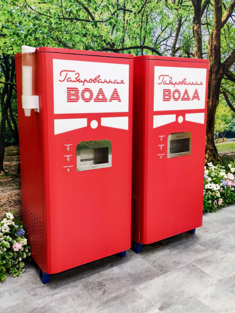 Пара автоматов газированной воды на фоне лесопарковой стилизации