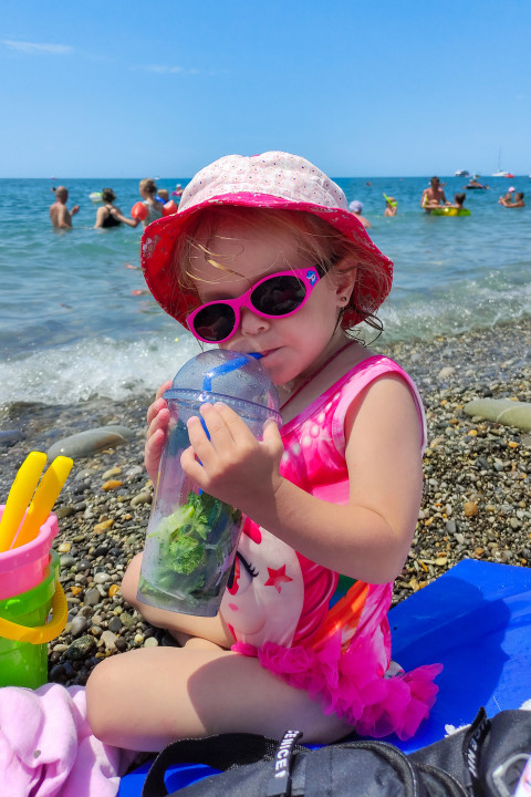 Девочка в солнцезащитных очках пьёт напиток на пляже