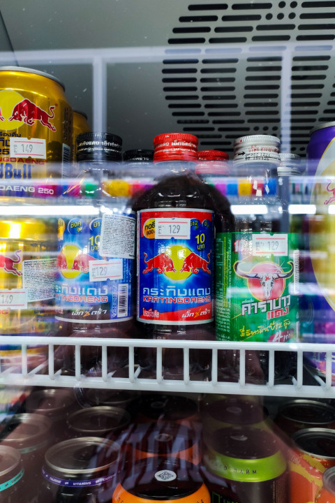 Энергетические напитки Red Bull и другие банки на полке холодильной витрины магазина