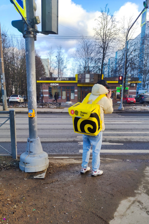 Курьер сервиса «Яндекс Еда» на городском перекрёстке