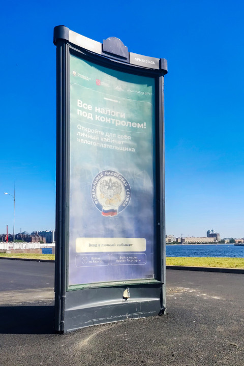 Рекламный стенд с плакатом ФНС на фоне Невы и летнего неба