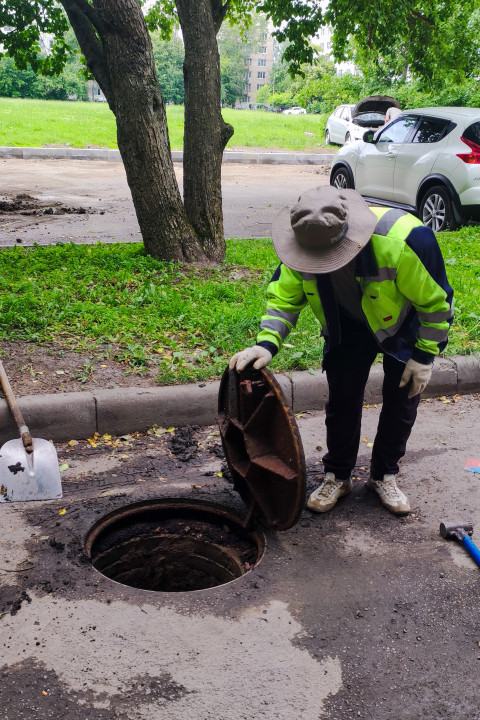 Работник в спецодежде открывает крышку люка на дворовой дороге
