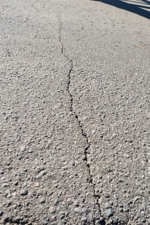 Крупный план трещины и крошки на асфальте с контрастной тенью от деревьев