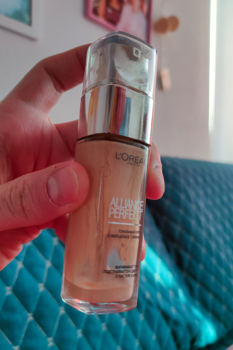 Флакон тонального крема L'Oreal Alliance Perfect в руке