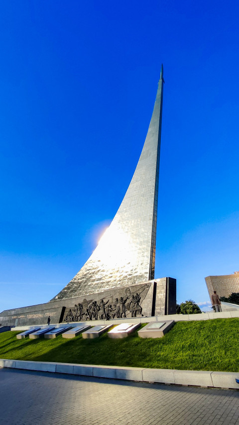 Монумент «Покорителям космоса» с барельефом у основания и отражением солнечного света