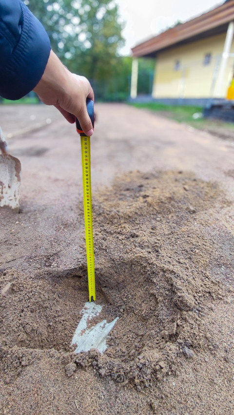 Измерение глубины песчаного слоя рулеткой на строительном объекте