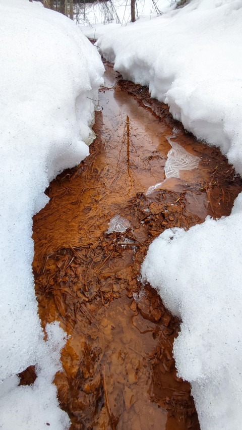 Талый ручей с рыжеватой водой среди снежных сугробов