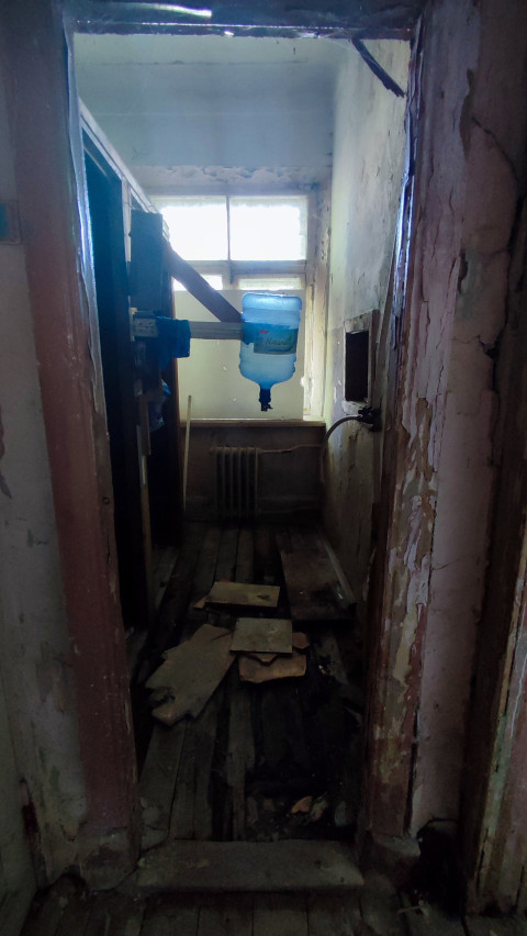 Узкое помещение с подвесной ёмкостью для воды и разрушенным полом