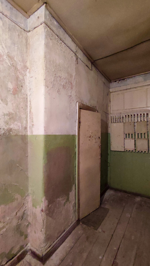 Облупившаяся стена с зелёной полосой и электрощитами в торце коридора