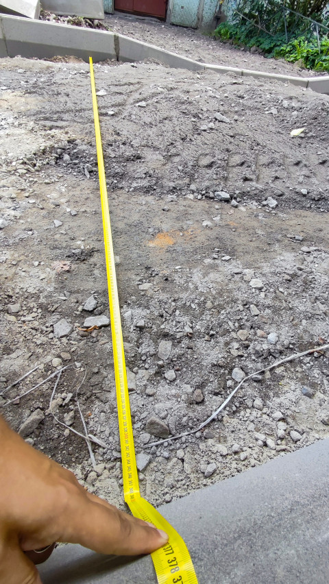 Измерение ширины подготовленного участка у бордюра строительной рулеткой на дворовой стройплощадке