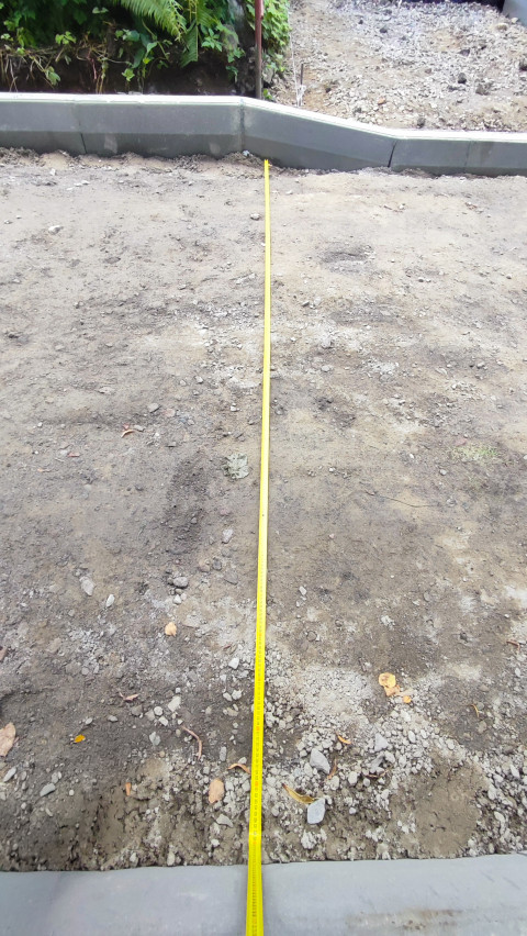 Замер расстояния рулеткой у углового поворота бордюрной линии на щебне