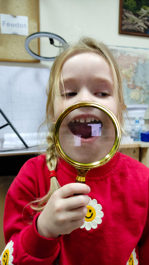 Девочка показывает рот через увеличительное стекло