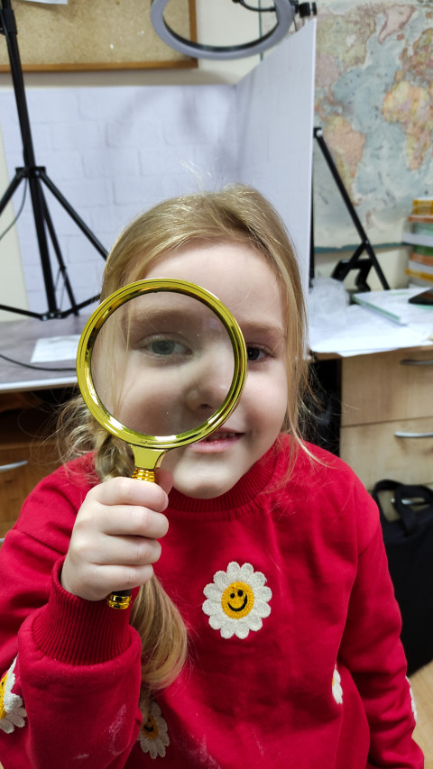 Девочка смотрит через увеличительное стекло в классе