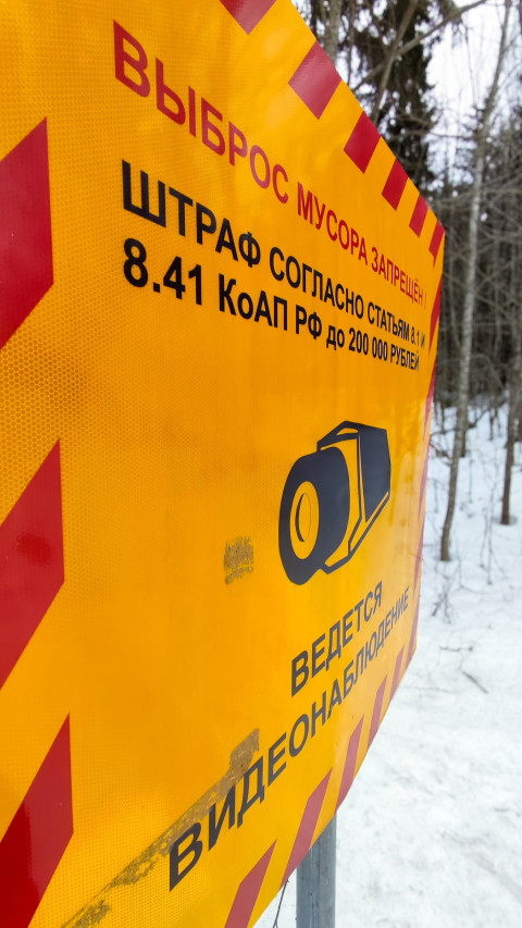 Дорожный знак о штрафе за выброс мусора и видеоконтроле в зимнем лесу