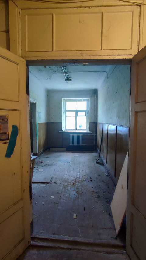 Коридор в старом здании с окном и радиатором, снятый через открытые двустворчатые двери