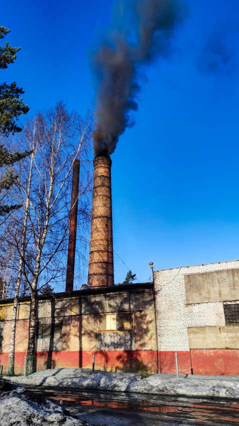 Кирпичная труба котельной с черным дымом на фоне синего неба