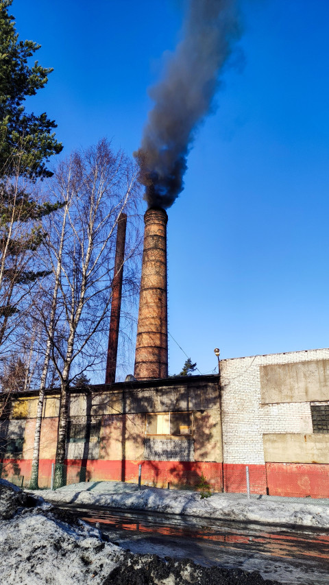Заводская труба с выбросами черного дыма в зимнее небо