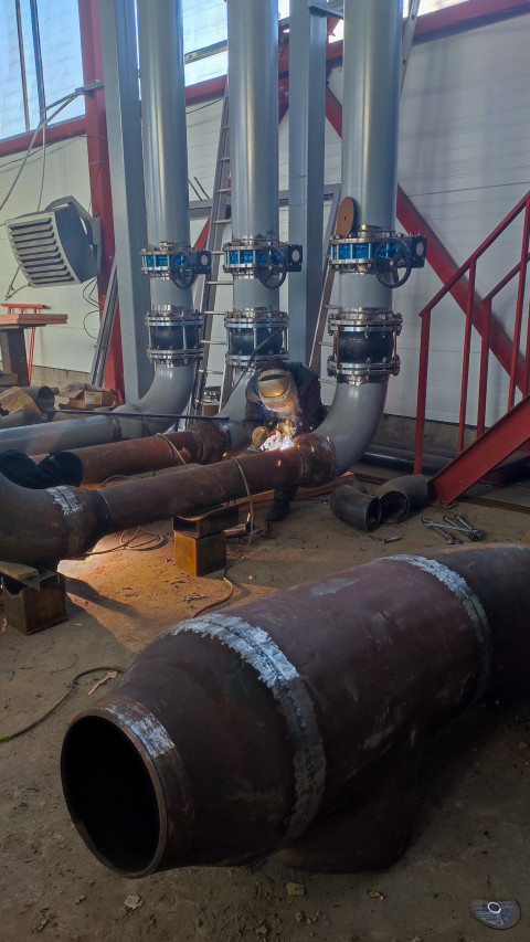Сварщик работает на трубопроводной системе внутри цеха