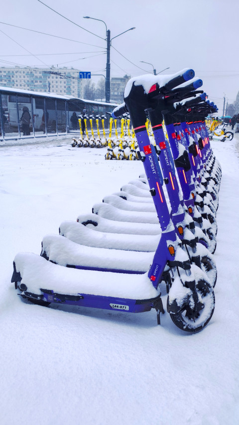 Линия фиолетовых электросамокатов Юрент под снегом на городской площадке