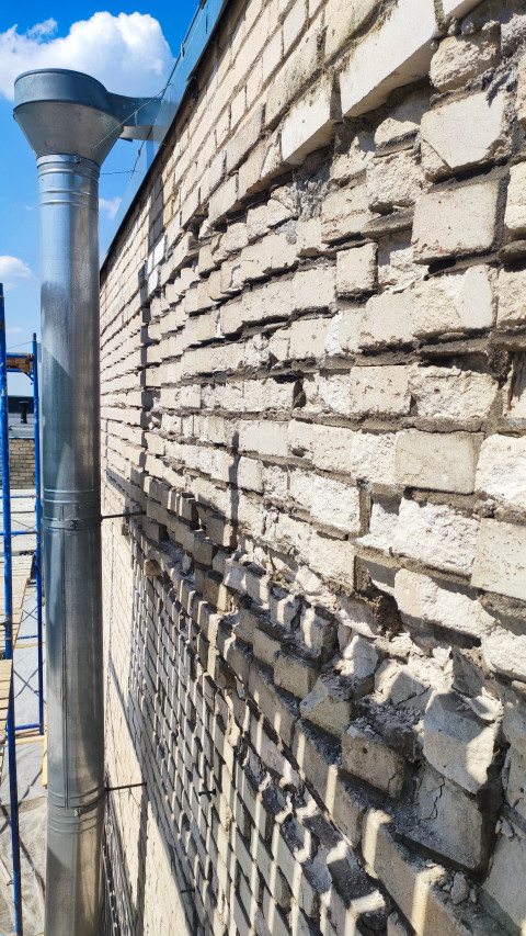 Дренажная труба на фоне повреждённой кирпичной стены здания
