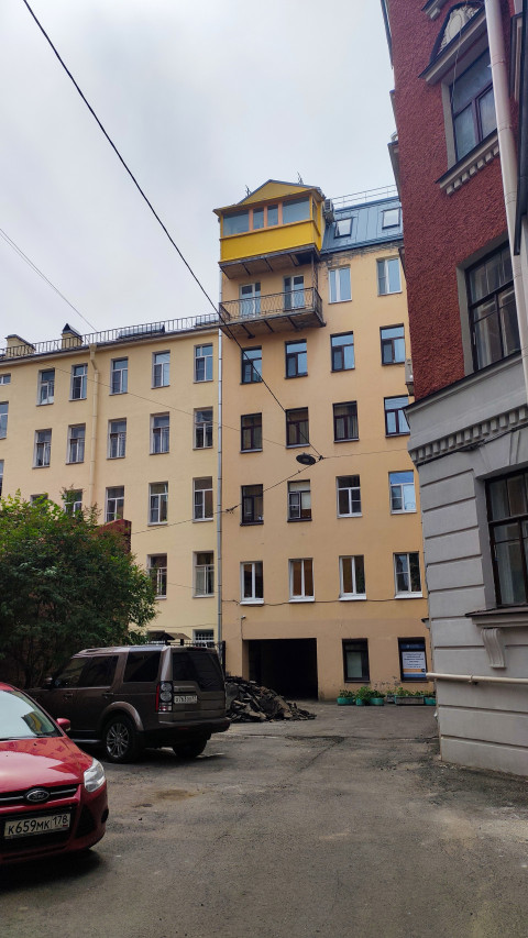 Парковка во внутреннем дворе с кучей снятого асфальта и фасадом дома с жёлтой мансардной надстройкой