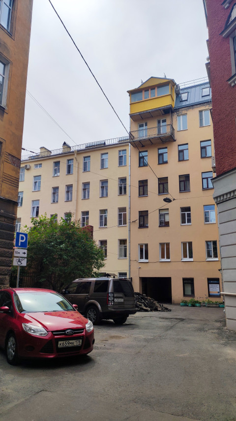 Двор жилого дома с арочным проездом, припаркованными автомобилями и надстройкой на крыше