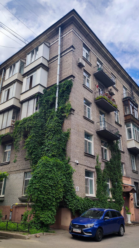 Кирпичная пятиэтажка с плющом на фасаде и воздушными проводами на фоне облаков