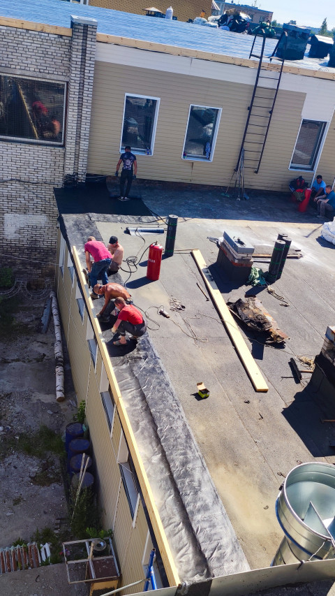 Рабочие наплавляют рулонную гидроизоляцию по кромке плоской кровли возле парапета