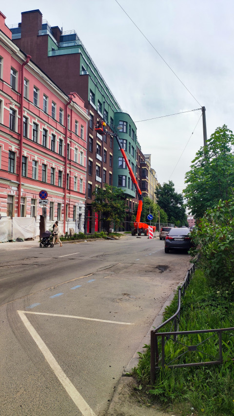 Автовышка у жилого дома и рабочий в корзине во время обслуживания фасада на городской улице