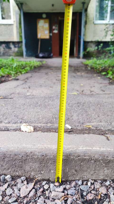 Замер высоты бордюра рулеткой перед входом в подъезд на дворовой дорожке