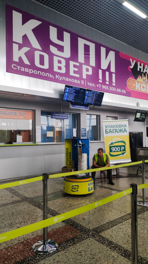 Сервис упаковки багажа в терминале с ценником и рекламными вывесками